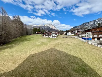 a large grass field with houses and mountains in the background at Charme alpino e modernità-Appartamento ristrutturato a due passi dal centro in Cortina dʼAmpezzo