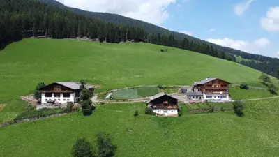 an aerial view of a large green hill with houses at Ortlerhof im Ultental - Urlaub auf dem Bauernhof in Ultimo