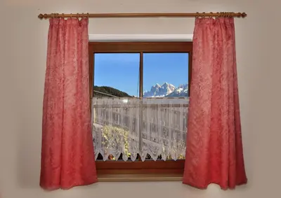 a window with red curtains and a view of a mountain at Schienhof in Chiusa