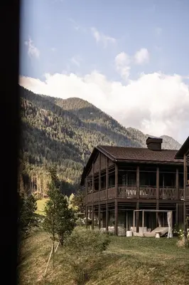 a large wooden house with mountains in the background at AMONTI Chalets in Molini di Tures