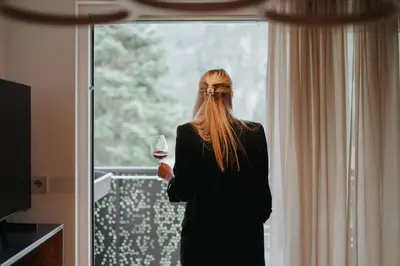 a woman holding a glass of wine looking out the window at Paradeis Apartments in Mühlbach