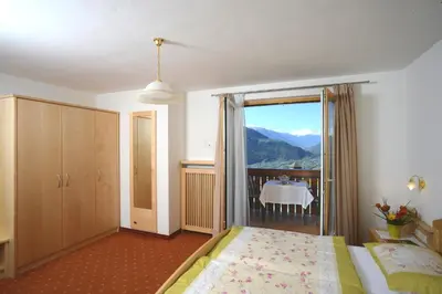 a bedroom with a bed and a balcony with a view at Garni Praidlerhof in Tirolo