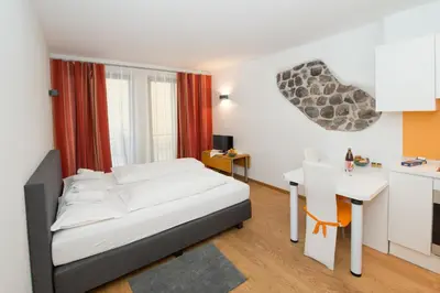 a bedroom with a bed and a table and a kitchen at Vintler Apartments in Bolzano