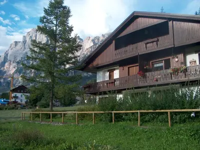 a large wooden house with a tree and a mountain at Villa Istria Apartment in San Vito di Cadore