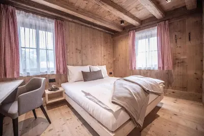a bedroom with a bed and a desk and windows at Ciasa Somuer in San Vigilio Di Marebbe