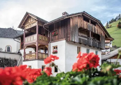 a building with a balcony and red flowers at Ciasa Somuer in San Vigilio Di Marebbe