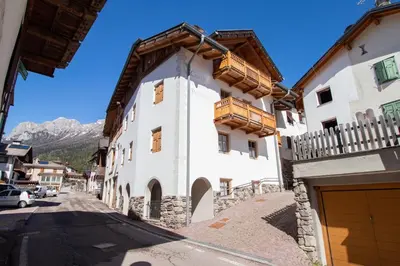 a white building with a wooden balcony on a street at Casa Podestà in Moena