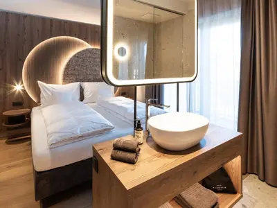 a bathroom with a sink and a bed with a mirror at Corones Suites - Dolomites Residence in Valdaora
