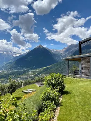a house on a hill with mountains in the background at Dahoam - Gardensuite R in Schenna