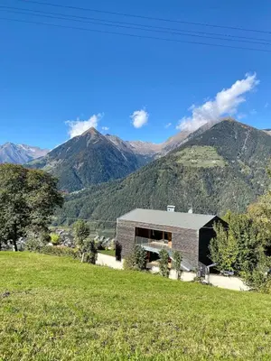 a house in a field with mountains in the background at Dahoam - Panoramchalet in Schenna