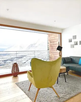 a living room with a green chair and a large window at Dahoam - Panoramchalet in Schenna
