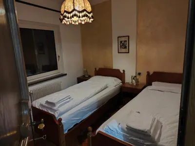 two beds in a room with a window and a chandelier at Casa Rizzi in Campitello di Fassa