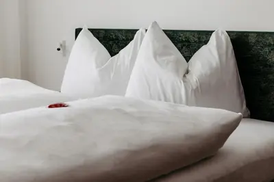a bed with white pillows on it with a red rose on it at Baumannhof in Sarntal