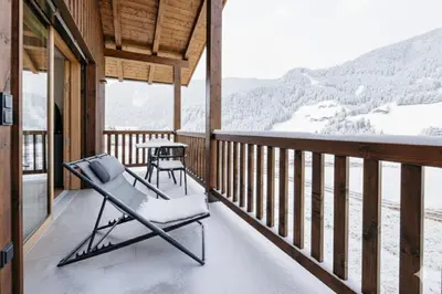 a porch with a chair and a table and snow covered mountains at Baumannhof in Sarntal