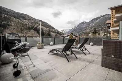 a person standing on a balcony with chairs and mountains at Panorama-Designapartment mit Kamin, Terrasse & Bergblick Nähe Sterzing - Villa Tribulaunblick in Colle Isarco
