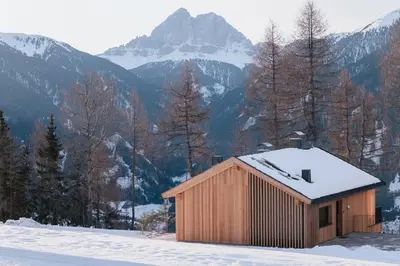a wooden building in the snow with mountains in the background at Chalet Herol in Luson