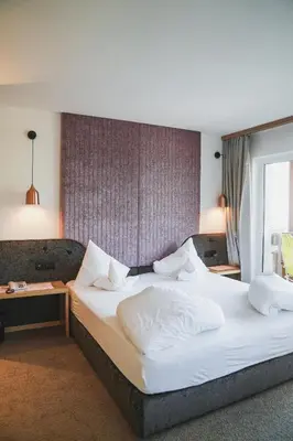 a hotel room with a bed with white sheets and pillows at Alpenpalais Kröll in Schenna