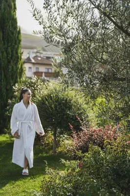 a woman in a white robe walking through a garden at Alpenpalais Kröll in Schenna