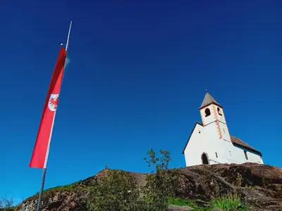 a church on top of a hill with a flag at FeWo Passo-Palade in Tesimo