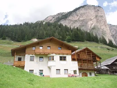 a house on a hill in front of a mountain at La Majon Apartments in Selva di Val Gardena