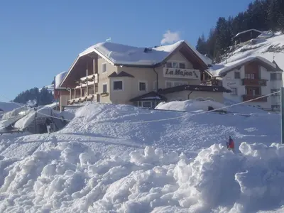 a snow covered slope in front of a ski lodge at La Majon Apartments in Selva di Val Gardena