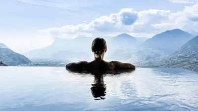 a woman sitting in the water looking at mountains at Hotel Gartner in Tirolo