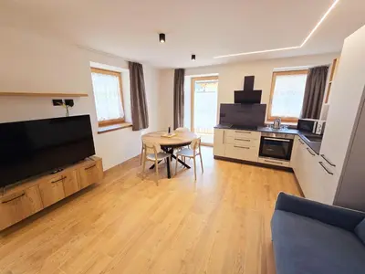 a living room with a kitchen with a table and a television at Alpine Lodge Tesero - Alpine Stay Apartments in Tesero