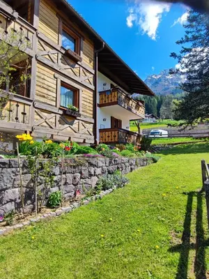 a wooden house with a stone retaining wall and a yard at Garofol da Mont-Dolomiti e Relax in Soraga