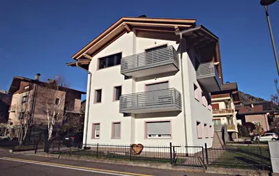 a white building with balconies on the side of a street at Guest House Cemin in Predazzo