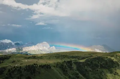 a rainbow over a green field with mountains at Rifugio Bec de Roces in Pallua
