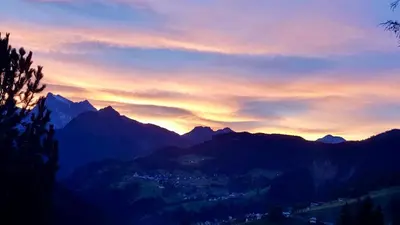 a sunset in the mountains with a city and mountains at Antler Apartment in Santa Fosca
