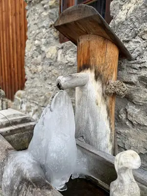 a stone building with a fountain with ice and a wooden practition at Silentium Dolomites Chalet in Monguelfo