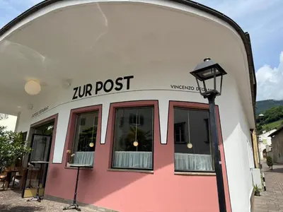 a pink and white building with a post sign on it at Hotel Zur Post in Egna