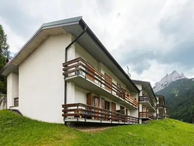 a building on a hill with mountains in the background at Apartment Casa Morelli by Interhome in Pozza di Fassa