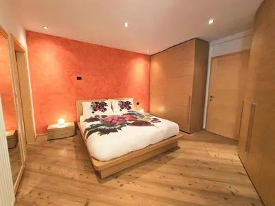 a bedroom with a bed with an orange wall at Essenze di Bosco - Alpine Stay Apartments in Predazzo
