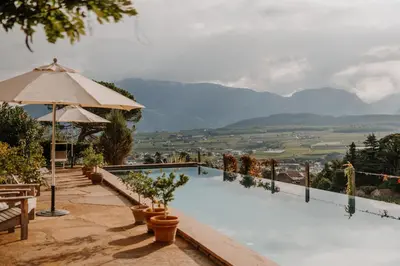 a pool with an umbrella and a view of the mountains at Schloss Englar in Appiano sulla Strada del Vino