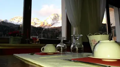 a table with glasses and plates and a window with mountains at Albergo al Sole in Val di Zoldo