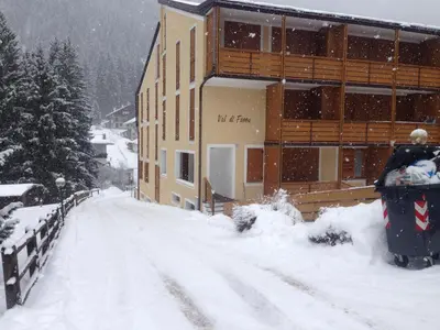 a snow covered road in front of a building at VAL DI FASSA CENTRAL HOUSE - Rooms with free parking in Canazei