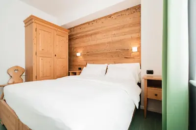 a bedroom with a white bed and a wooden wall at Hotel Oasi in Cortina dʼAmpezzo