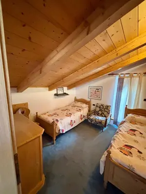 a attic room with two beds and a chair at Pragma Apartments - Casa Defrancesco in Cavalese