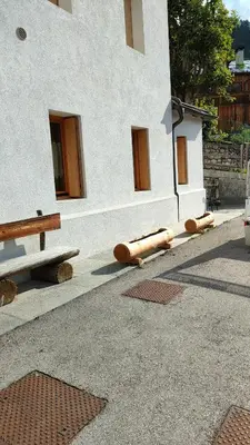 a building with wooden logs on the ground next to a bench at Sunny and cosy holiday apartment in the Dolomites in Pianaz