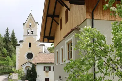 a church with a clock tower next to a building at Berg Apartment Vajolet - Unterweger Berg Apartments in Tisens