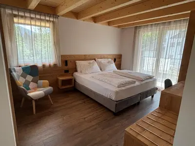 a bedroom with a bed and a chair and windows at Fiemme in Vista in Ziano di Fiemme