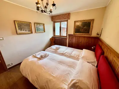 a bedroom with a white bed with a chandelier at Villa Anna apartment - Center view - in Cortina dʼAmpezzo