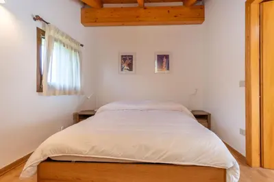 a bedroom with a bed with white sheets and a window at Casa dei Gigli in Selva di Cadore