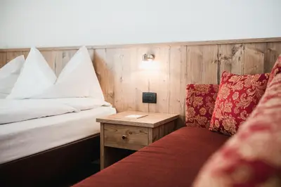 a room with a bed and a table with a red couch at Laguscei Dolomites Mountain Hotel in Arabba