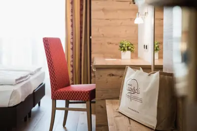 a room with a bed and a chair and a bag at Laguscei Dolomites Mountain Hotel in Arabba