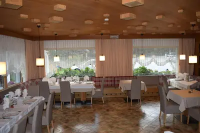 a dining room with tables and chairs and windows at Hotel Crepes de Sela in Campitello di Fassa