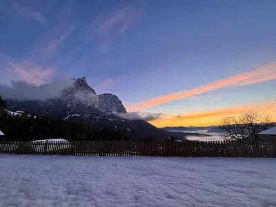 a snow covered yard with a fence and a mountain at AppartmentPircher 2 in Siusi