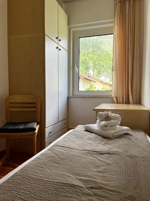 a bedroom with a bed with a window and a chair at Appartamento Le Sipole in Ziano di Fiemme